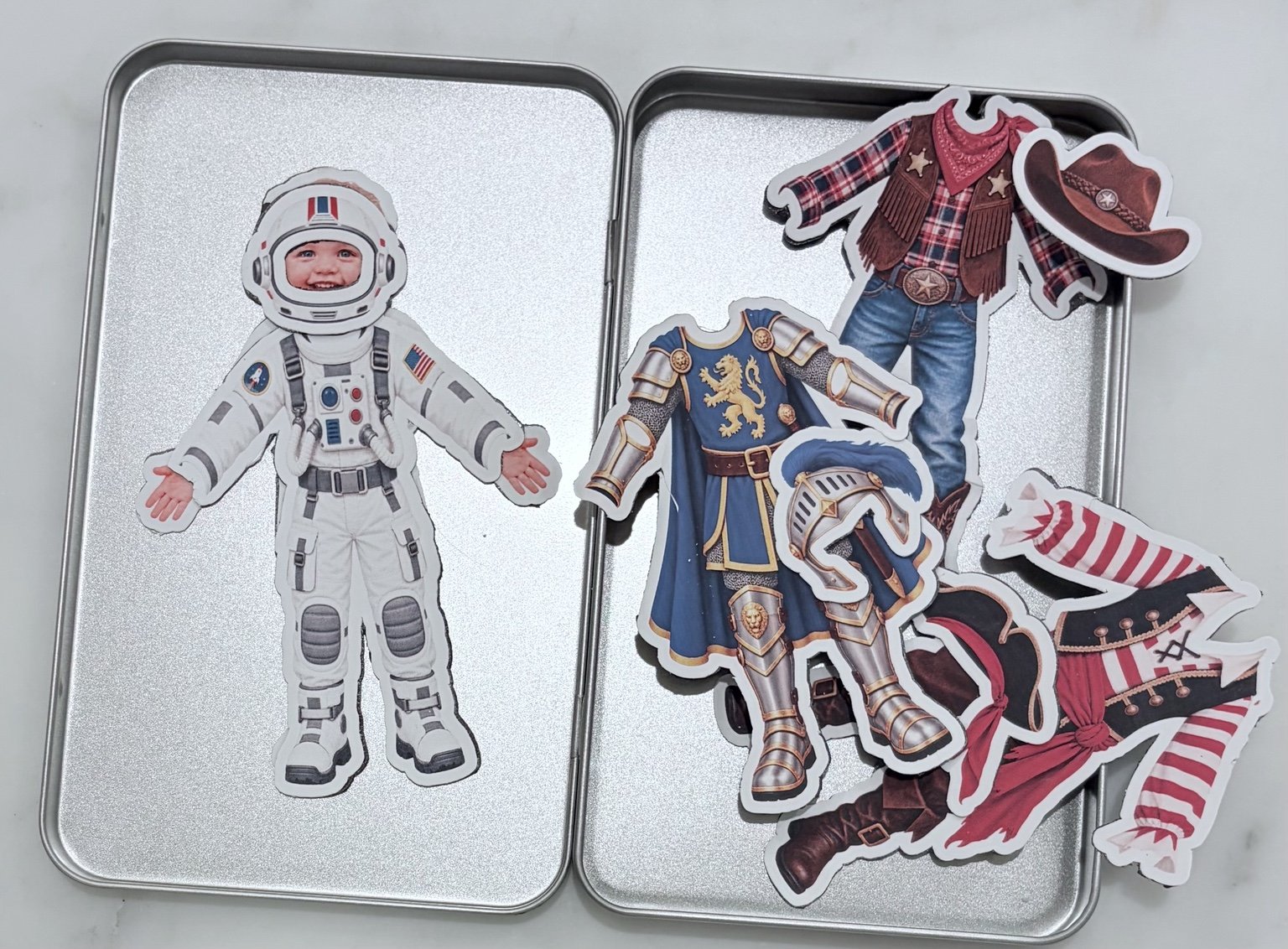 Boy doll wearing astronaut outfit alongside dress-up costumes in tin